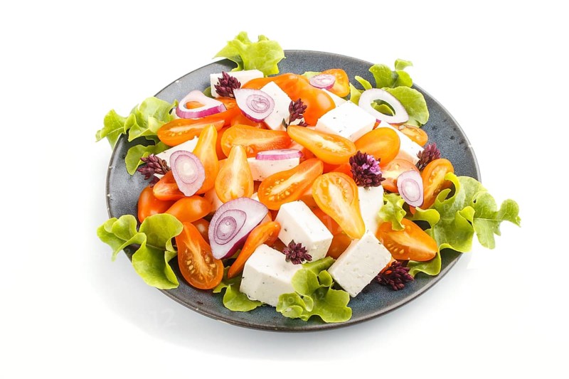 Vegetarian salad with fresh grape tomatoes, feta cheese, lettuce and onion on blue ceramic plate isolated on white background, side view, close up