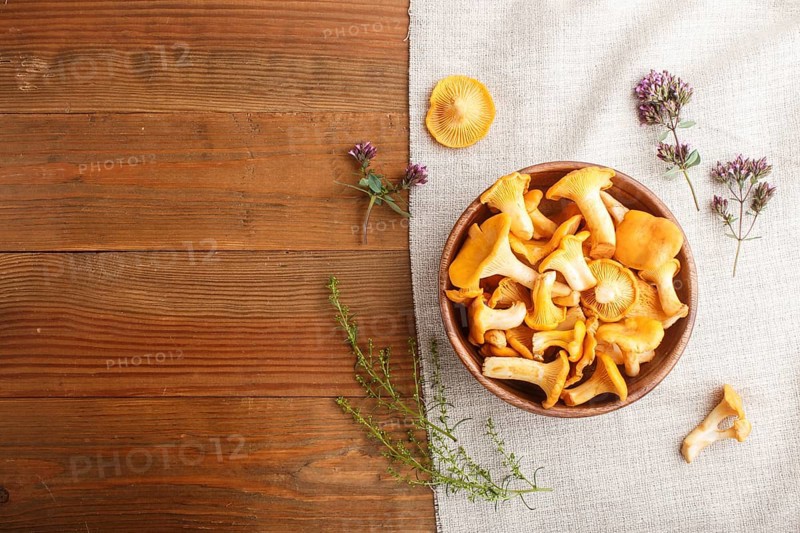 Chanterelle mushrooms in wooden bowl and spice herbs on wooden background with linen textile. top view, copy space, flat lay