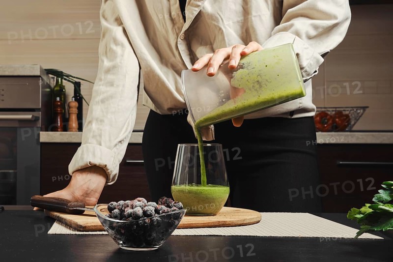 Unrecognizable woman pouring green smoothie in glass in the kitchen