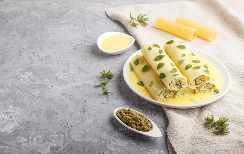 Cannelloni pasta with egg sauce, cream cheese and oregano leaves on a gray concrete background with linen textile. side view, close up, copy space