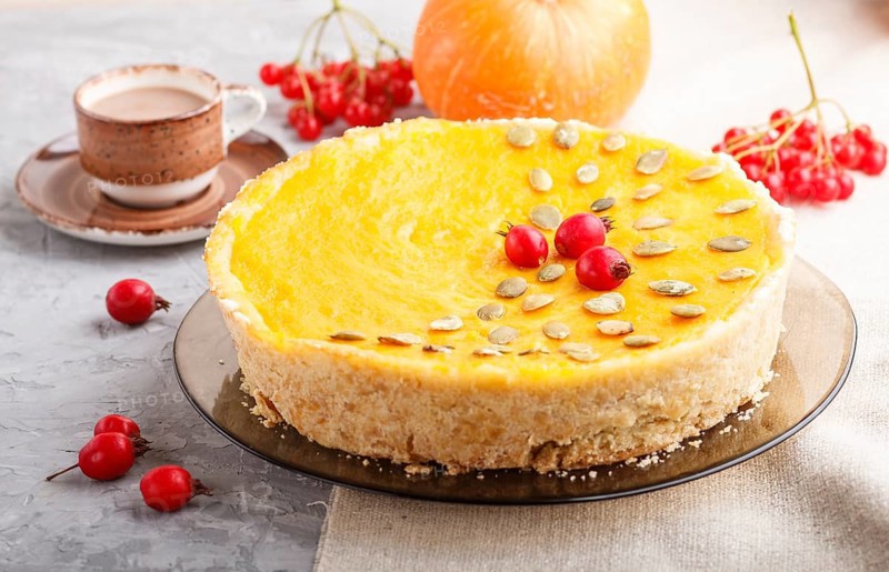 Traditional american sweet pumpkin pie decorated with hawthorn red berries and pumpkin seeds with cup of coffee on a gray concrete background. side view, close up, selective focus
