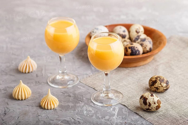 Sweet egg liqueur in glass with quail eggs and meringues on a gray concrete background. Side view, close up