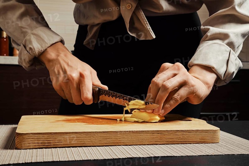 Unrecognizable woman slicing peeled ginger root into thin strips