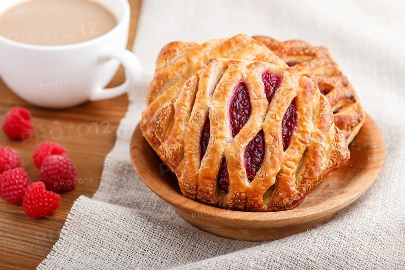 Puff pastry buns with strawberry jam on wooden background with linen textile and a cup of coffee. side view, close up, selective focus