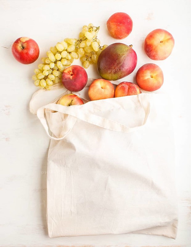 Fruits in reusable cotton textile white bag. Zero waste shopping, storage and recycling concept, eco friendly lifestyle. Top view, flat lay, copy space. Peach, apple, mango, grape