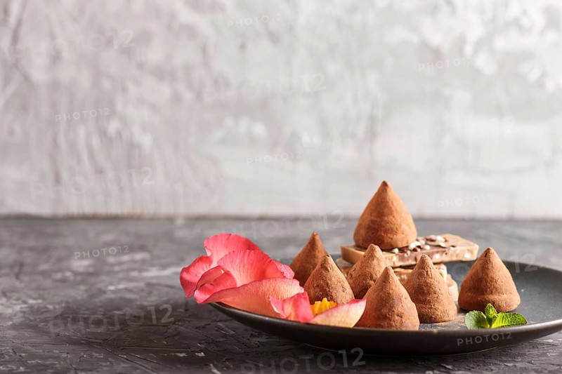 Chocolate truffle on blue ceramic plate decorated with rose petals on black concrete background. close up, side view. copy space