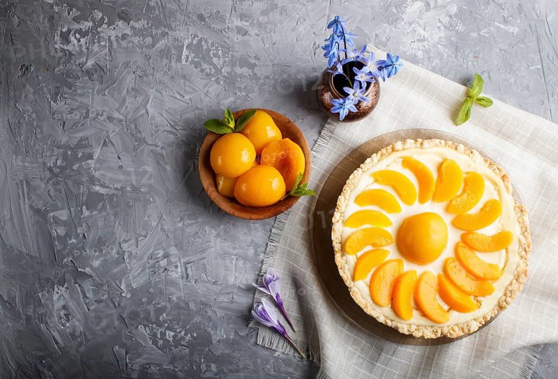 Round peach cheesecake and ceramic vase with blue flowers on a linen napkin on a gray concrete background. top view, copy space