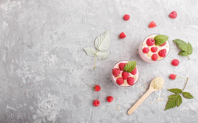 Yoghurt with raspberry and sesame in a glass and wooden spoon on gray concrete background. top view, flat lay, copy space