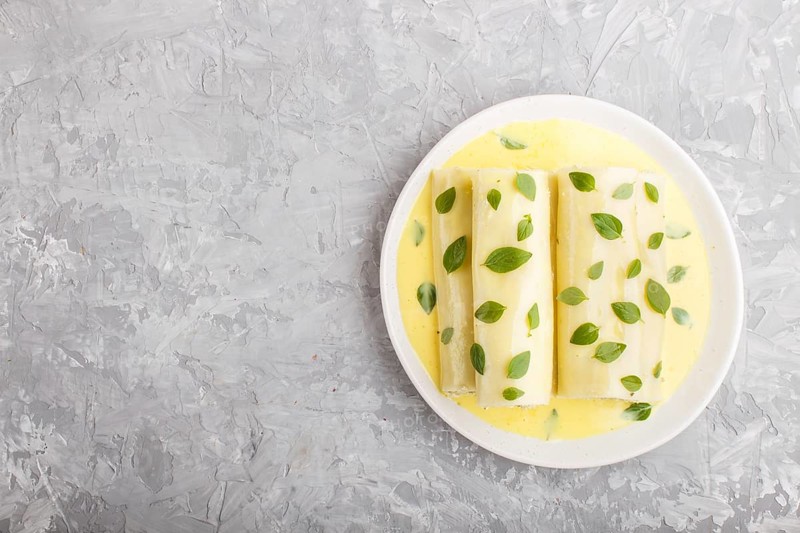 Cannelloni pasta with egg sauce, cream cheese and oregano leaves on a gray concrete background. top view, flat lay, copy space