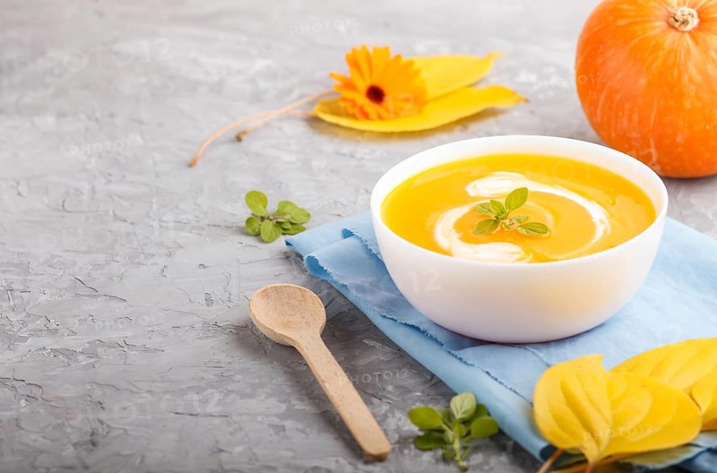 Traditional pumpkin cream soup with in white bowl on a gray concrete background with blue napkin. side view, close up, selective focus, copy space