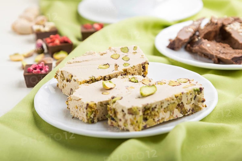 Traditional arabic sweets sesame halva with chocolate and pistachio and a cup of coffee on green textile background. side view, close up, selective focus