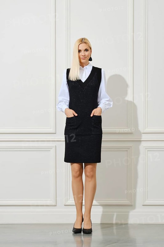 Cute woman in school uniform with hands in pockets next to white wall