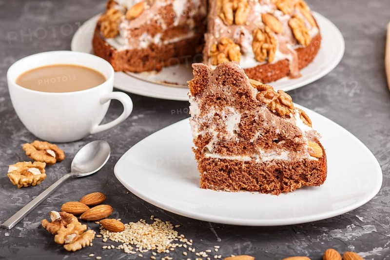 Homemade cake with milk cream, cocoa, almond, hazelnut on a black concrete background and a cup of coffee. Side view, close up, selective focus