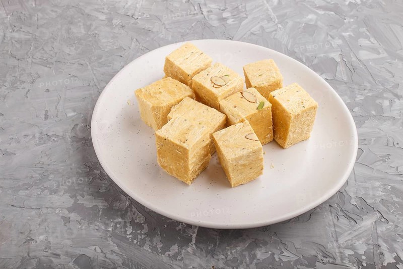 Traditional indian candy soan papdi in white plate with almond and pistache on a gray concrete background. side view, close up