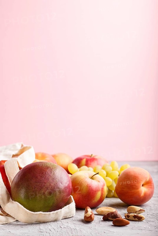 Fruits in reusable cotton textile white bag. Zero waste shopping, storage and recycling concept, eco friendly lifestyle. Side view, close up, copy space. Peach, apple, nuts, mango, grape