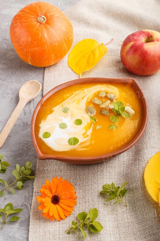 Traditional pumpkin cream soup with seeds in clay bowl on a gray concrete background with linen textile. side view, close up