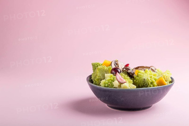 Vegetarian salad from romanesco cabbage, champignons, cranberry, avocado and pumpkin on a pastel pink background. side view, copy space