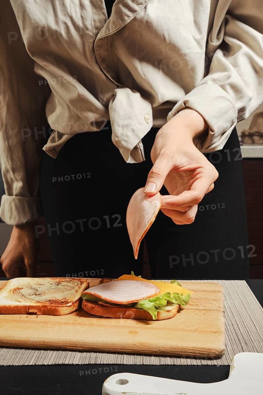 Unrecognizable woman puts slice of ham on sandwich