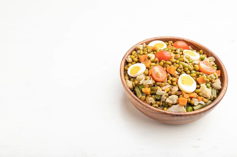 Mung bean porridge with quail eggs, tomatoes and microgreen sprouts on a white wooden background. Side view, close up, copy space
