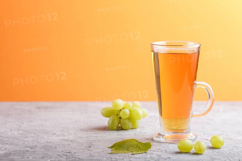 Glass of green grape juice on a gray and orange background. Morninig, spring, healthy drink concept. Side view, copy space