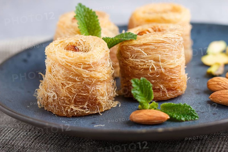 Kunafa, traditional arabic sweets in blue ceramic plate on a gray concrete background. side view, close up, selective focus