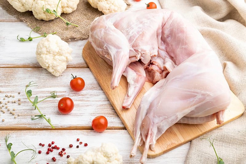 Whole raw rabbit with cauliflower, tomatoes and spices on a white wooden background and linen textile. Side view, close up, selective focus