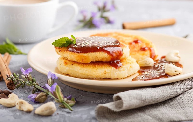 Cheese pancakes with caramel sauce on a beige ceramic plate and a cup of coffee on a gray concrete background. side view, close up