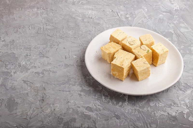 Traditional indian candy soan papdi in white plate with almond and pistache on a gray concrete background. side view, copy space