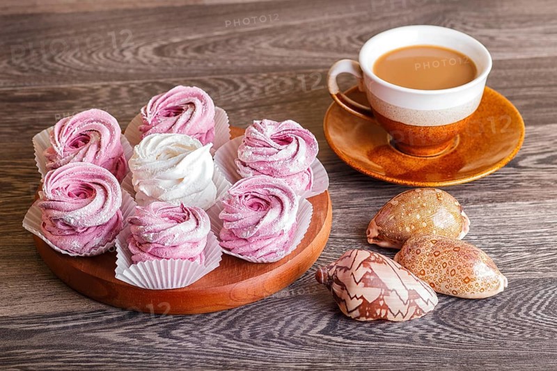 Pink and white homemade marshmallows (zephyr) on a round wooden board with cup of coffee and seashells on a gray wooden background