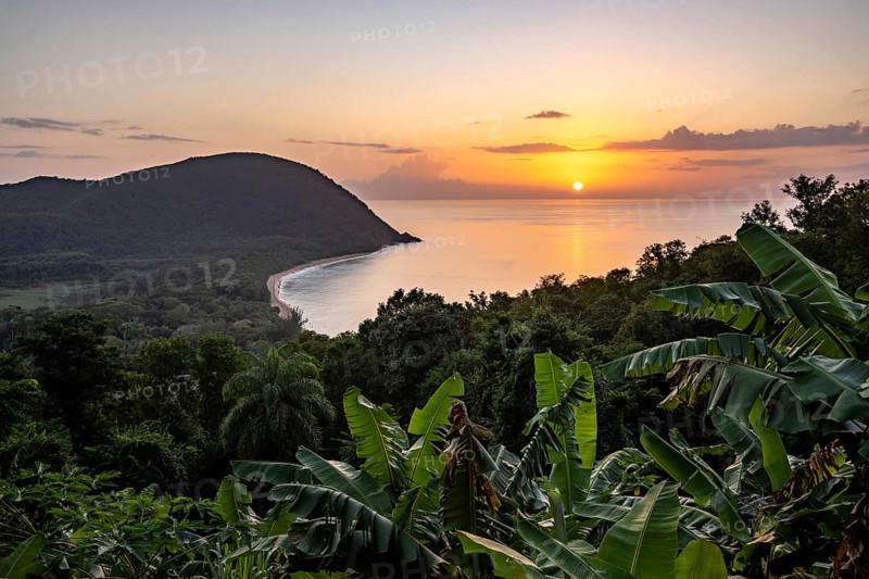 View from a mountain to a secluded bay with a sandy beach and mangrove forest. The sun rises over the sea and bathes the surroundings in a golden light. Grande Anse beach, Basse Terre, Guadeloupe, French Antilles, Caribbean, North America