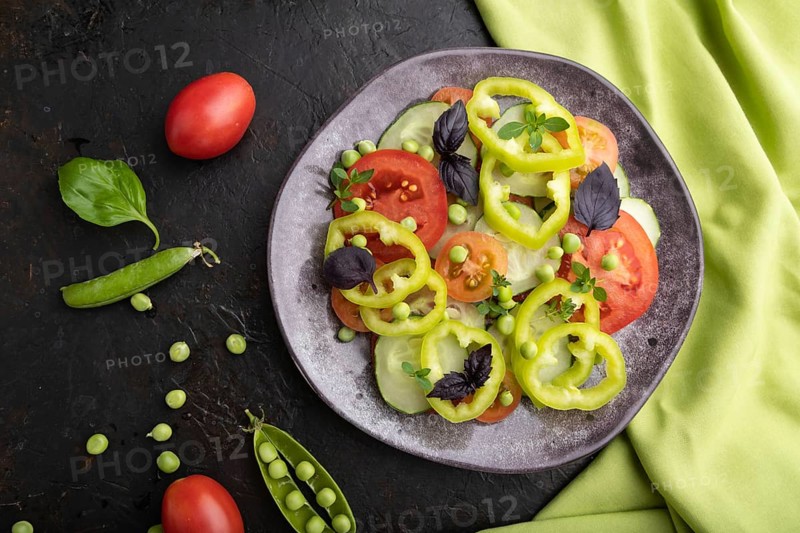 Vegetarian salad from green pea, tomatoes, pepper and basil on a black concrete background and green textile. top view, close up, flat lay