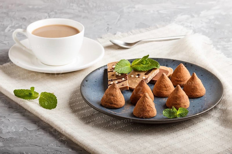 Chocolate truffle on blue ceramic plate and a cup of coffee on gray concrete background. close up, side view