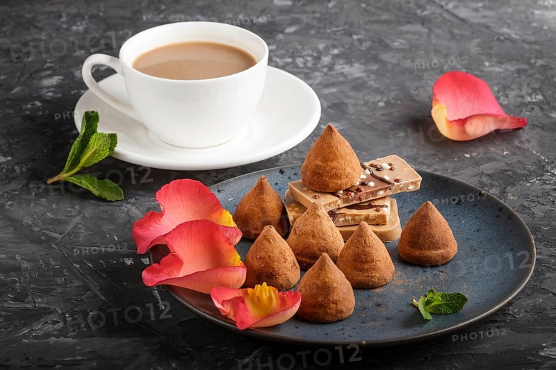 Chocolate truffle on blue ceramic plate decorated with rose petals and a cup of coffee on black concrete background. close up, side view