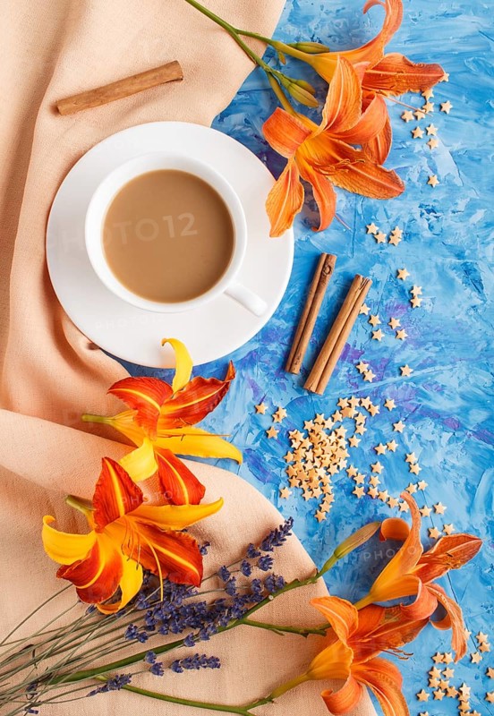 Orange day-lily and lavender flowers and a cup of coffee on a blue concrete background, with orange textile. Morninig, spring, fashion composition. Flat lay, top view, close up