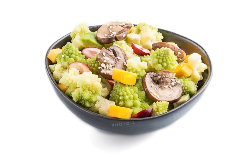 Vegetarian salad from romanesco cabbage, champignons, cranberry, avocado and pumpkin in black bowl isolated on a white background. side view, close up