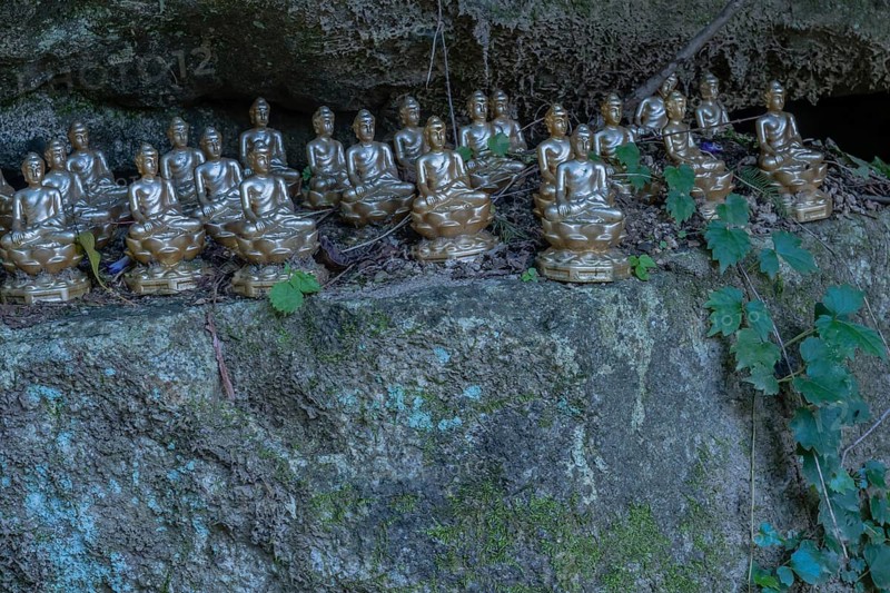 Miniature sitting Buddhas on ledge of boulder in mountainous public park in South Korea