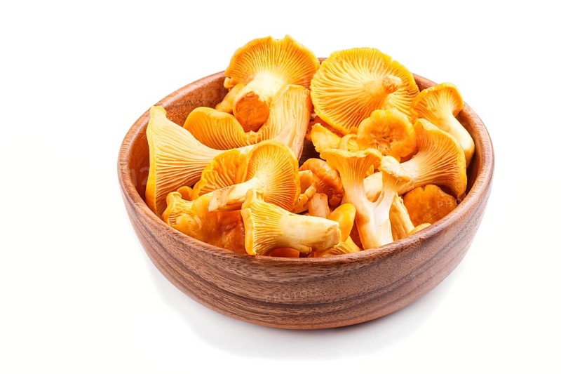 Bunch of chanterelle mushrooms in wooden bowl isolated on white background. side view, close up