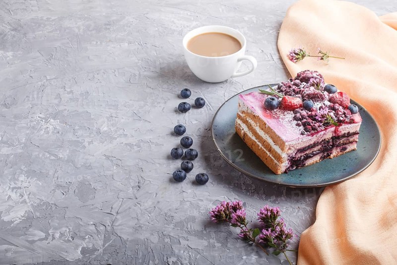 Berry cake with milk cream and blueberry jam on blue ceramic plate with cup of coffee and fresh blueberries on a gray concrete background with orange textile. side view, copy space