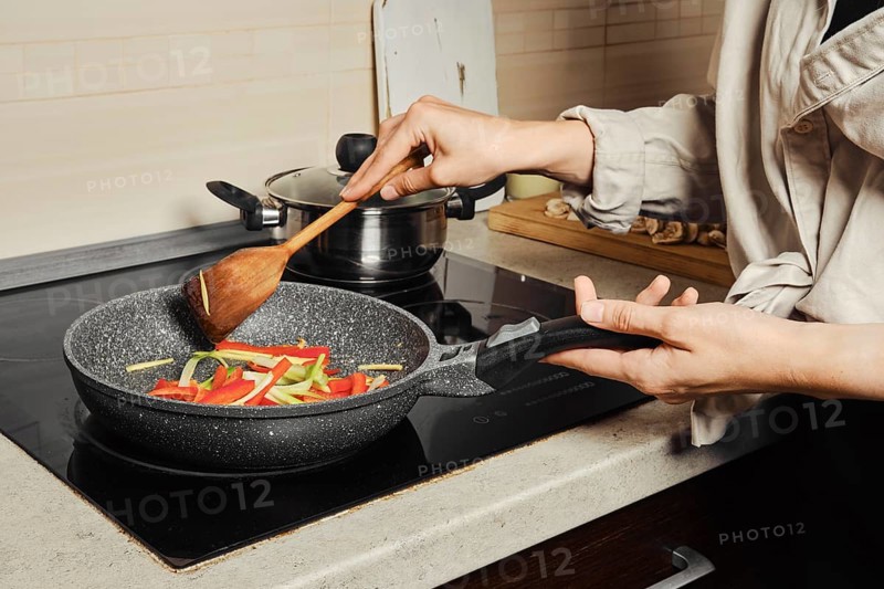 Unrecognizable woman stirring vegetable dressing with wooden spatula in frying pan