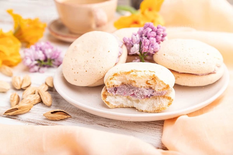 Meringues cakes with cup of coffee on a white wooden background and orange linen textile. Side view, close up, selective focus