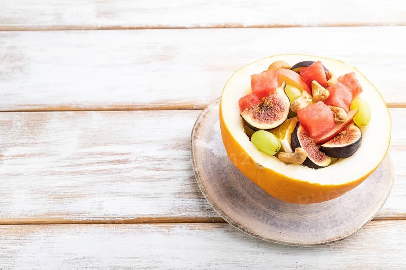 Vegetarian fruit salad of watermelon, grapes, figs, pear, orange, cashew on white wooden background. Side view, copy space, close up