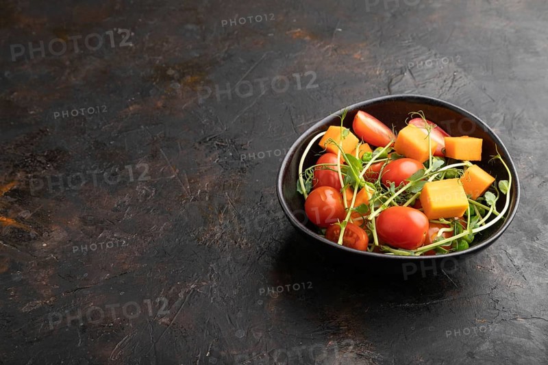 Vegetarian vegetable salad of tomatoes, pumpkin, microgreen pea sprouts on black concrete background. Side view, copy space, close up