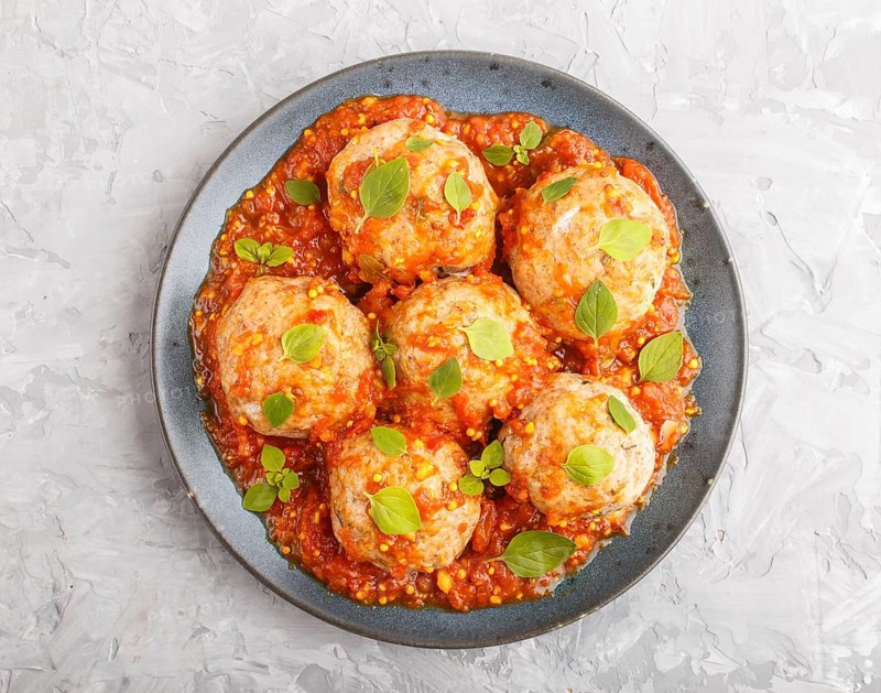 Pork meatballs with tomato sauce, oregano leaves, spices and herbs on blue ceramic plate on a gray concrete background. top view, flat lay, close up