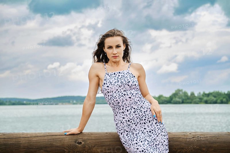 Cute woman in sundress leaning on wooden fence of a pier