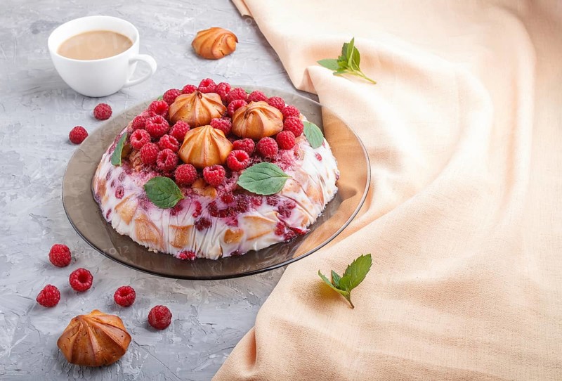 Homemade jelly cake with milk, cookies and raspberry on a gray concrete background with cup of coffee and orange textile. side view. copy space