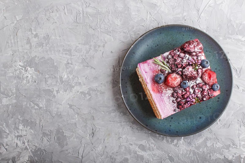 Berry cake with milk cream and blueberry jam on blue ceramic plate on a gray concrete background. top view, flat lay, copy space