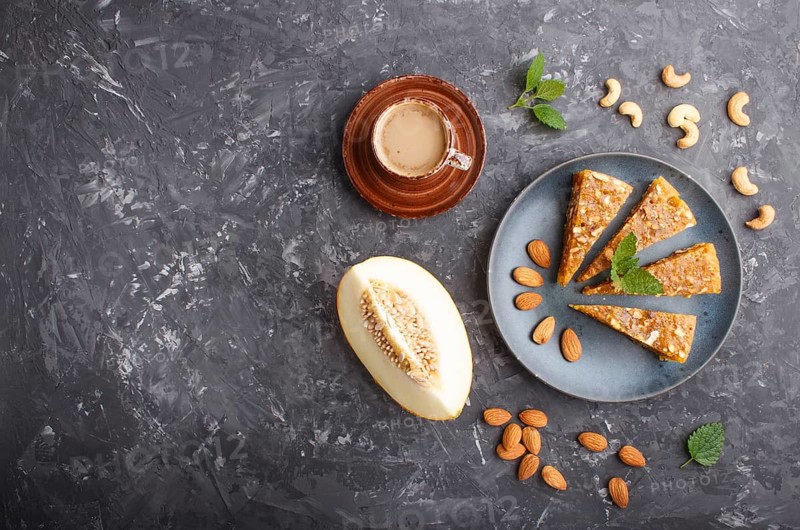 Traditional turkish candy cezerye made from caramelised melon, roasted walnuts, hazelnuts, cashew, pistachios in blue ceramic plate and a cup of coffee on a black concrete background. top view, flat lay, copy space