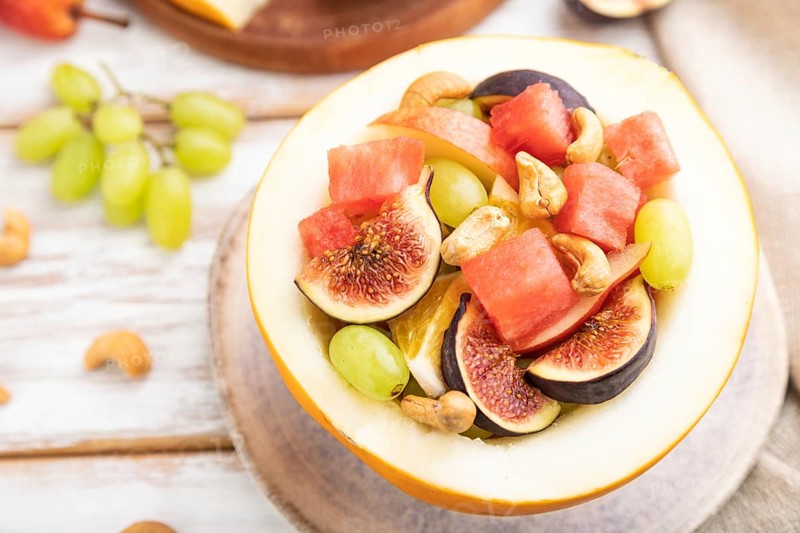 Vegetarian fruit salad of watermelon, grapes, figs, pear, orange, cashew on white wooden background and linen textile. Side view, close up, selective focus