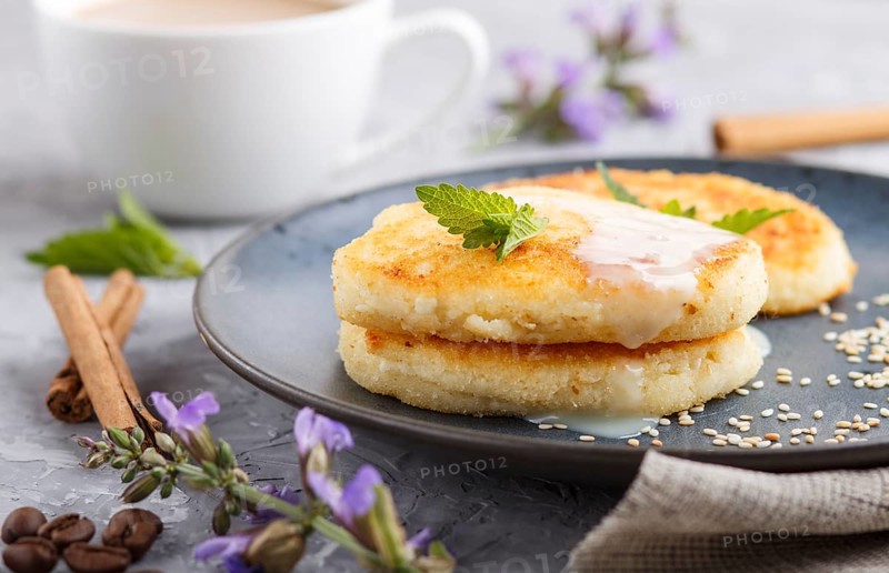 Cheese pancakes on a blue ceramic plate and a cup of coffee on a gray concrete background. side view, close up
