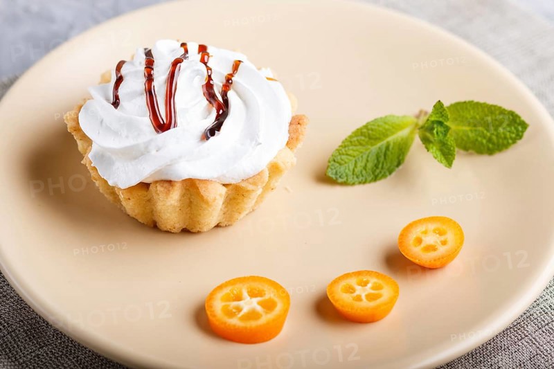 Cake with whipped egg cream on a light brown plate with kumquat slices and mint leaves on a gray concrete background with linen napkin. selective focus, close up. side view